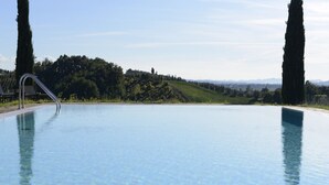 Ein weitläufiger, klarer Pool mit einer Metallleiter, umgeben von üppiger, grüner Natur und hohen Bäumen.
