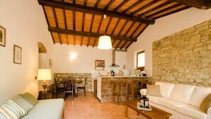 A cozy room with a bed, a sofa, a wooden coffee table, a stone wall, a kitchen area with a bar, and a hanging light fixture. - Agriturismo Poggio di Montepescoli - Il Ciliegio (Pelago (fi))