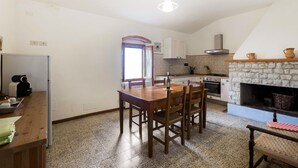 A kitchen with a stone fireplace, a dining table with chairs, and a refrigerator. - Agriturismo Poggio di Montepescoli - Il Ciliegio (Pelago (fi))