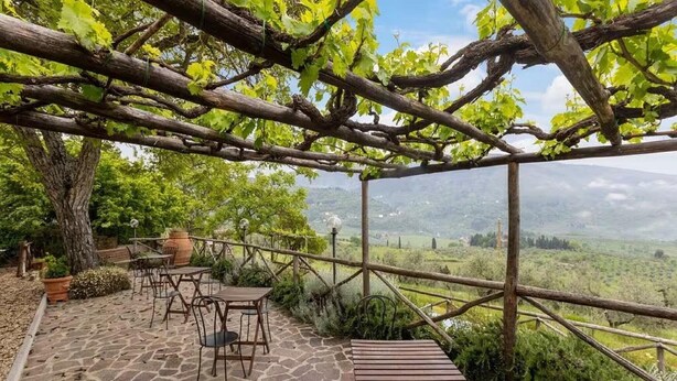 A covered outdoor seating area with stone flooring, wooden tables, and chairs, overlooking a scenic landscape. - Agriturismo Poggio di Montepescoli - Il Ciliegio (Pelago (fi))