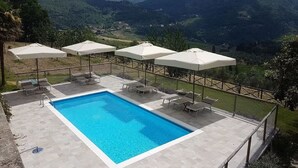 A rectangular pool with lounge chairs and umbrellas, surrounded by a fence, with a mountainous landscape in the background. - Agriturismo Poggio di Montepescoli - Il Ciliegio (Pelago (fi))