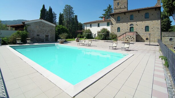 Une piscine avec des chaises longues, des bâtiments en pierre et une tour.