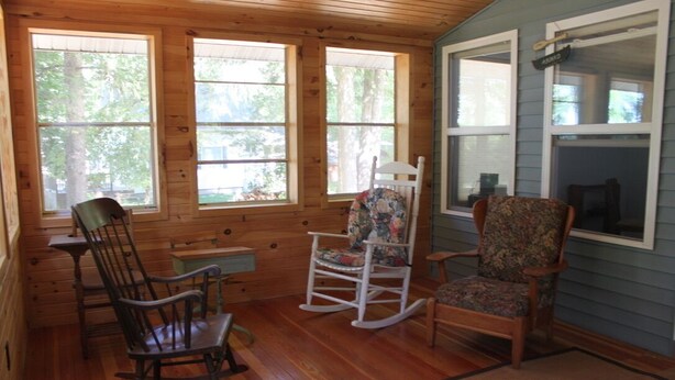A cabin interior with wooden walls and floors, two rocking chairs, a small table, and large windows offering a view of trees. - Restored 1920's peaceful, lakeside cottage (Pullman)