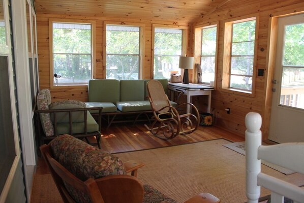 A cozy cabin interior with a green sofa, rocking chair, and a small table with a lamp.
