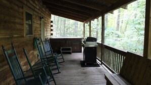 Una cabaña de madera con porche, una parrilla al aire libre y varios sillones mecedores.