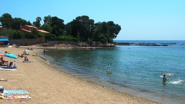 A beach with people sunbathing and swimming, a clear sky, and a rocky shoreline. - Saint Raphael plage Peguiere (Saint Raphäel)
