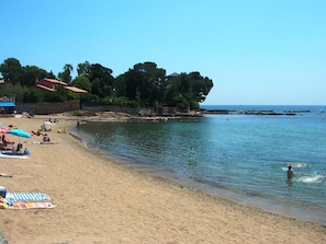A beach with people sunbathing and swimming, a clear sky, and a rocky shoreline.