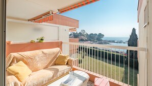 A balcony with a beige sofa, a small table with a glass, and a view of the sea. - Saint Raphael plage Peguiere (Saint Raphäel)