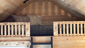 A loft-style bedroom with a sloped ceiling, wooden bunk beds, and a ladder. - Whispering Winds Cabin - cozy double loft cabin (Pickardville)