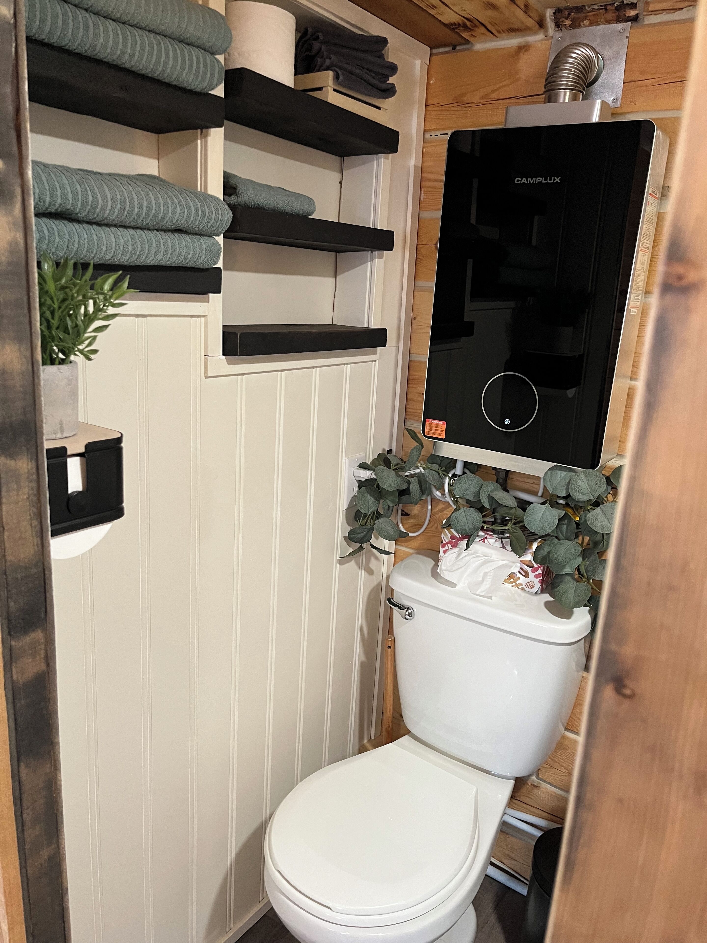 Une petite salle de bain avec des toilettes blanches, des étagères avec des serviettes, un radiateur et une plante en pot.