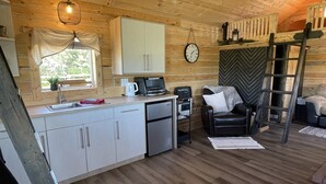 A compact kitchen with a sink, a toaster, and a refrigerator. There is a wooden ceiling and a window with curtains. - Whispering Winds Cabin - cozy double loft cabin (Pickardville)