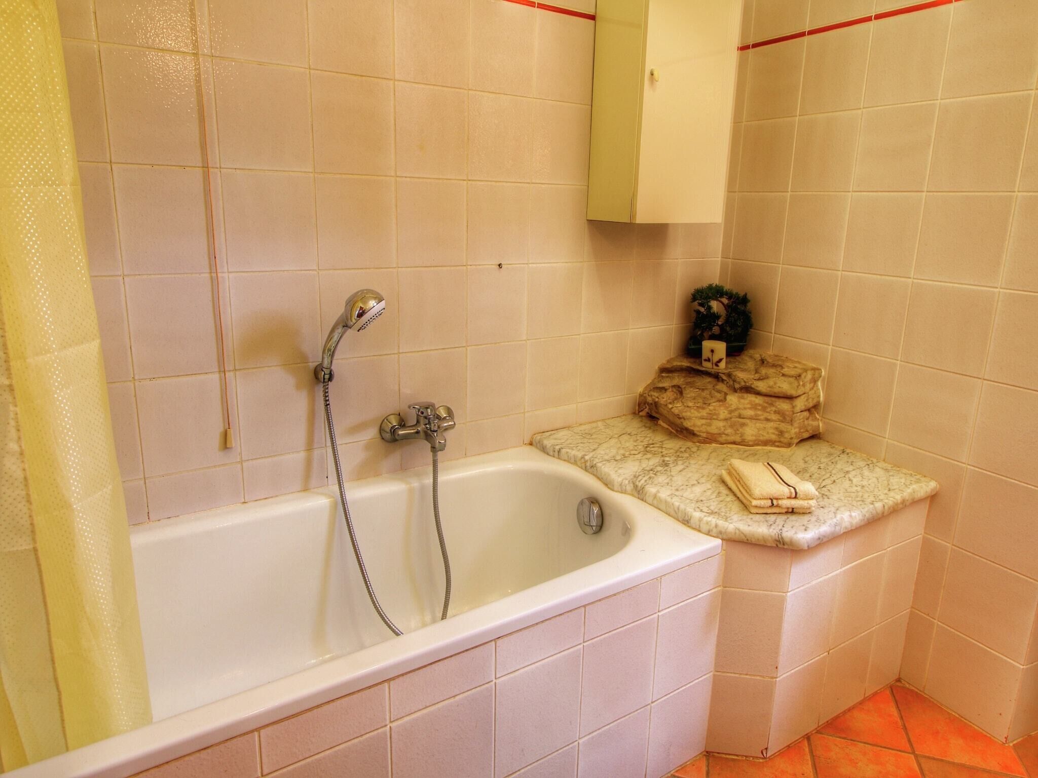 Une salle de bain équipée d’une baignoire, d’une douche et d’une petite étagère où sont rangés les articles de toilette.