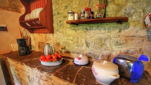 Un comptoir de cuisine avec un pare-feu en pierre, une machine à café, un bol de tomates, un récipient alimentaire hermétique, un bocal décoratif et un appareil électroménager bleu.