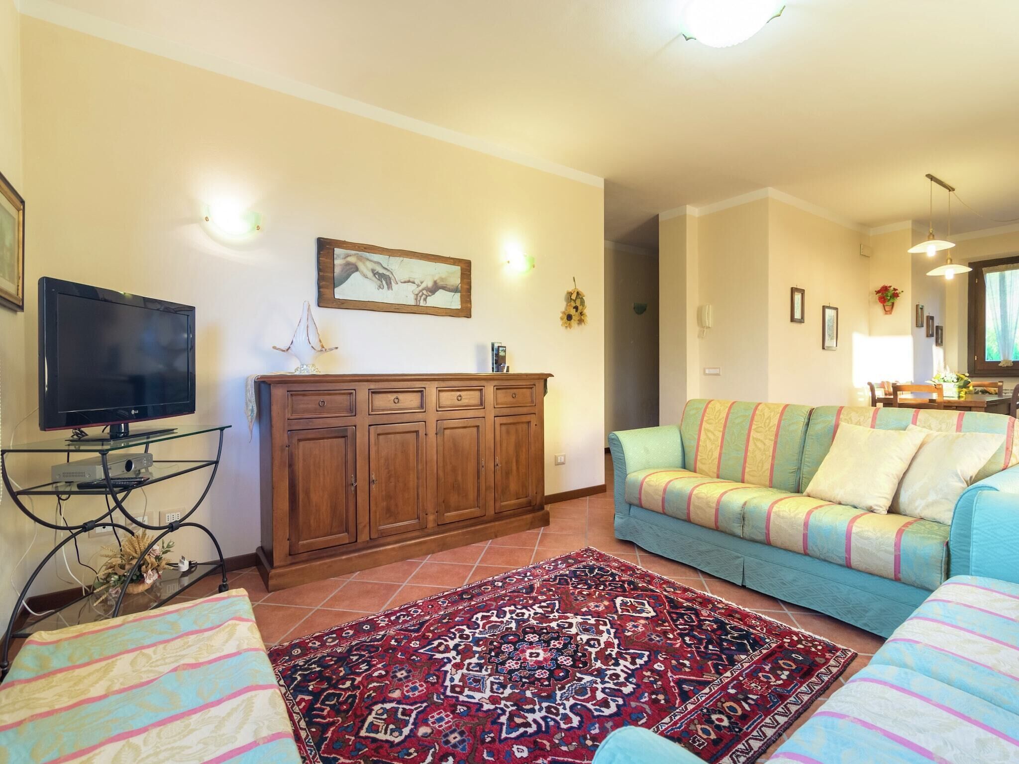 A living room with a flat-screen TV, wooden cabinet, colorful sofa, and patterned rug.