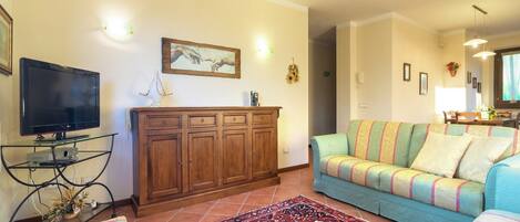 A living room with a flat-screen TV, wooden cabinet, colorful sofa, and patterned rug.