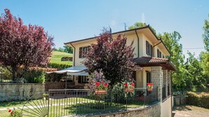A two-story house with a stone facade, a tiled roof, and a fenced garden with red flowers and trees. - Villa in Lonnano with pool (Lonnano)