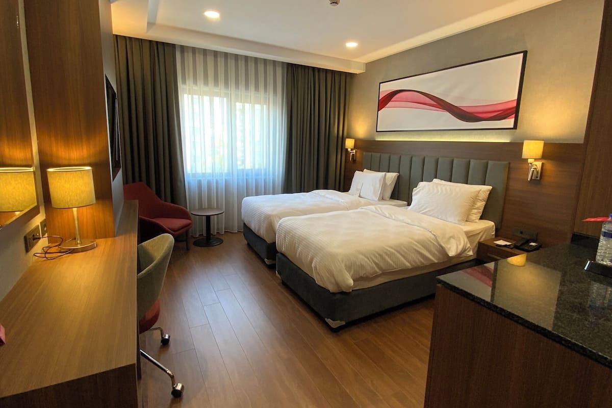 A hotel room with two beds, a desk, a chair, a small table, and a large abstract painting on the wall.