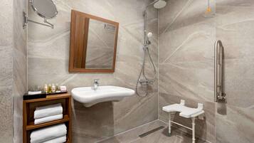Un baño moderno con pared de mármol, tocador de madera con toallas, lavamanos, espejo, ducha con cabezal de ducha manual y barra de apoyo.