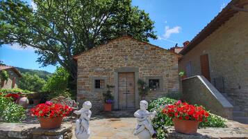 Un edificio in pietra con una porta di legno, vasi con fiori rossi e statue di pietra.