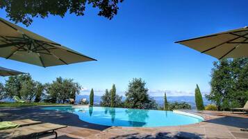 Una piscina con lettini e ombrelloni, immersa nel verde e sotto un cielo sereno.