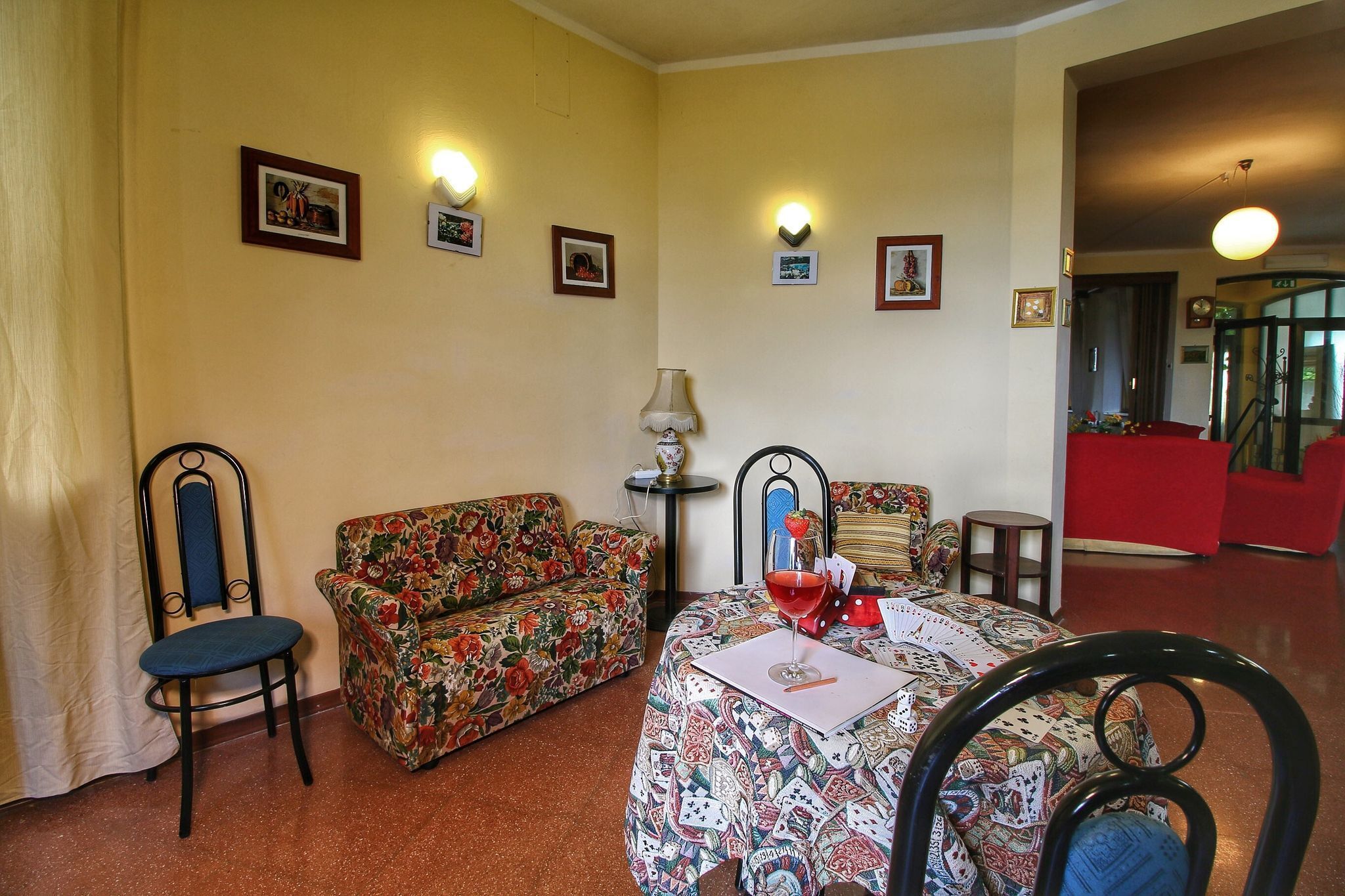 A living room with a floral sofa, a dining table with a card game, and a chair.