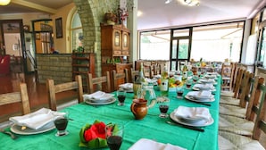 A long dining table set with green tablecloth, white napkins, plates, and glasses, surrounded by wicker chairs.