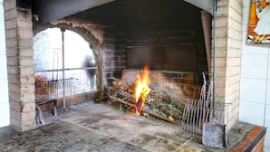 A fireplace with a fire burning inside, surrounded by brick walls and a metal grate.