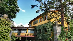 A yellow building with a balcony, surrounded by greenery and a cobblestone path.
