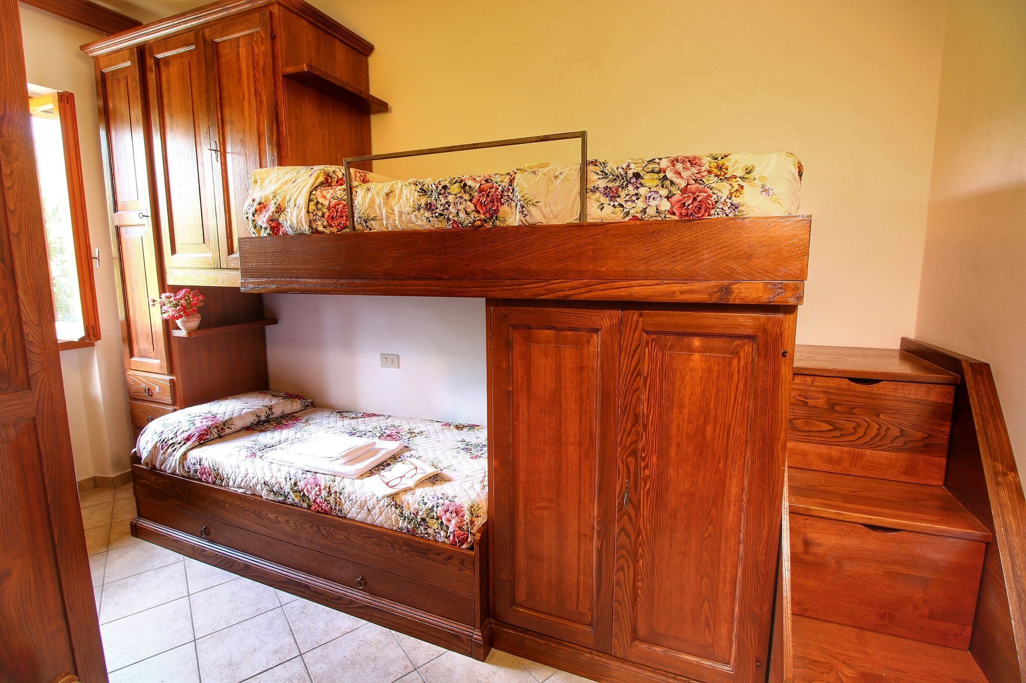 A bunk bed with a wooden frame, a floral bedspread, and a small bedside table with a vase.