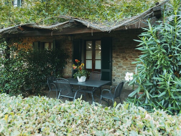 Un bâtiment en pierre avec un toit de chaume, une table entourée de chaises et des plantes en pot.