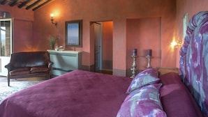 A bedroom with a large bed, a chair, a vanity with a mirror, and two wall sconces. - Villa with Pool and Wine Country Charm (Arezzo)