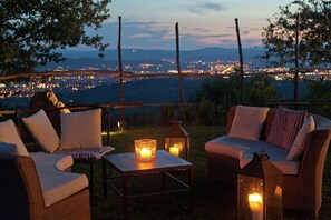Un área de estar al aire libre con mobiliario de mimbre y velas, con vista a un paisaje urbano al atardecer.
