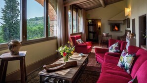A cozy living room with a fireplace, red sofas, and a large window overlooking greenery.