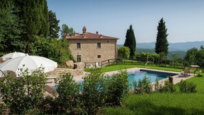 A stone villa with a swimming pool, surrounded by lush greenery and mountains in the background.