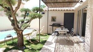 An outdoor patio with a pool, a grill, and a dining area with chairs and a table.