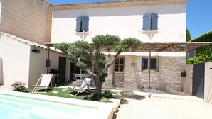 A villa with a swimming pool, a covered patio, and a garden with a tree.