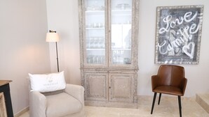 A room with a beige armchair, a brown leather chair, a cabinet with glass doors, and a wall with a 'Love Camis' sign.