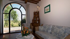 A cozy living room with a large arched window, a wooden bookshelf, a patterned sofa, and a table with a vase of flowers. - Tuscan Hilltop Farm Stay (Castelnuovo Berardenga)