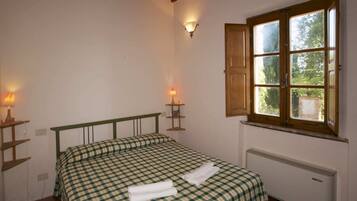 Une chambre à coucher avec un lit, deux lampes de chevet, une fenêtre donnant sur un espace verdoyant et un radiateur.