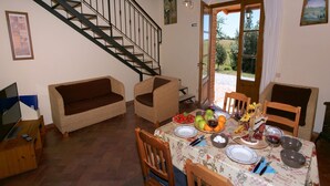 Comedor con mesa dispuesta para cuatro personas, rodeada de sillas de madera, un sofá y una escalera.