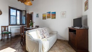 Ein gemütliches Wohnzimmer mit Sofa, Esstisch aus Holz, Stühlen, einem Fernseher und Kunstwerken an den Wänden.