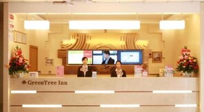 A reception desk at GreenTree Inn with two staff members, a TV screen, and a floral arrangement.