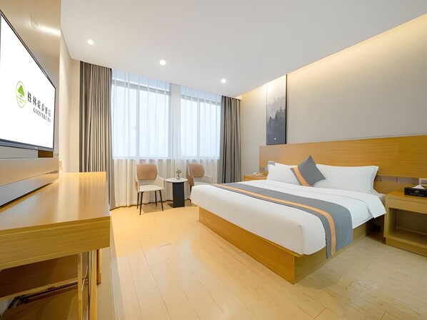 A hotel room with a bed, a desk, two chairs, a small table, and a TV.