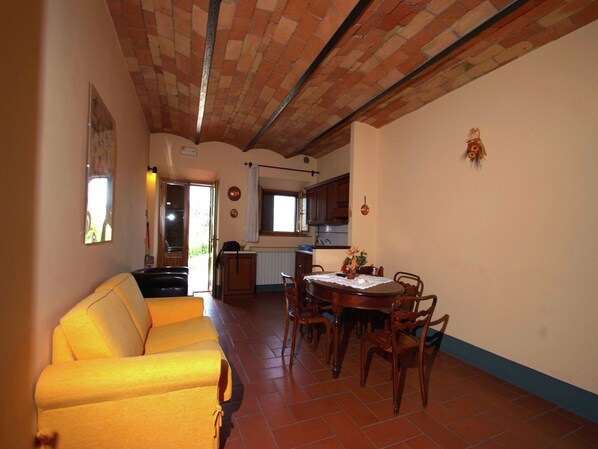 A dining area with a round table and chairs, a sofa, and a kitchen in the background. - Peaceful Pienza Garden Escape (Pienza)