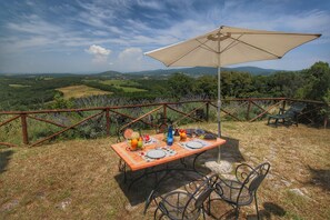 Uma área de refeições ao ar livre com uma mesa posta para dois, rodeada por uma cerca de metal, com vista para uma paisagem deslumbrante.