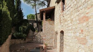 Edificio de piedra con un patio que cuenta con una mesa y sillas, rodeado de muros de piedra y vegetación.