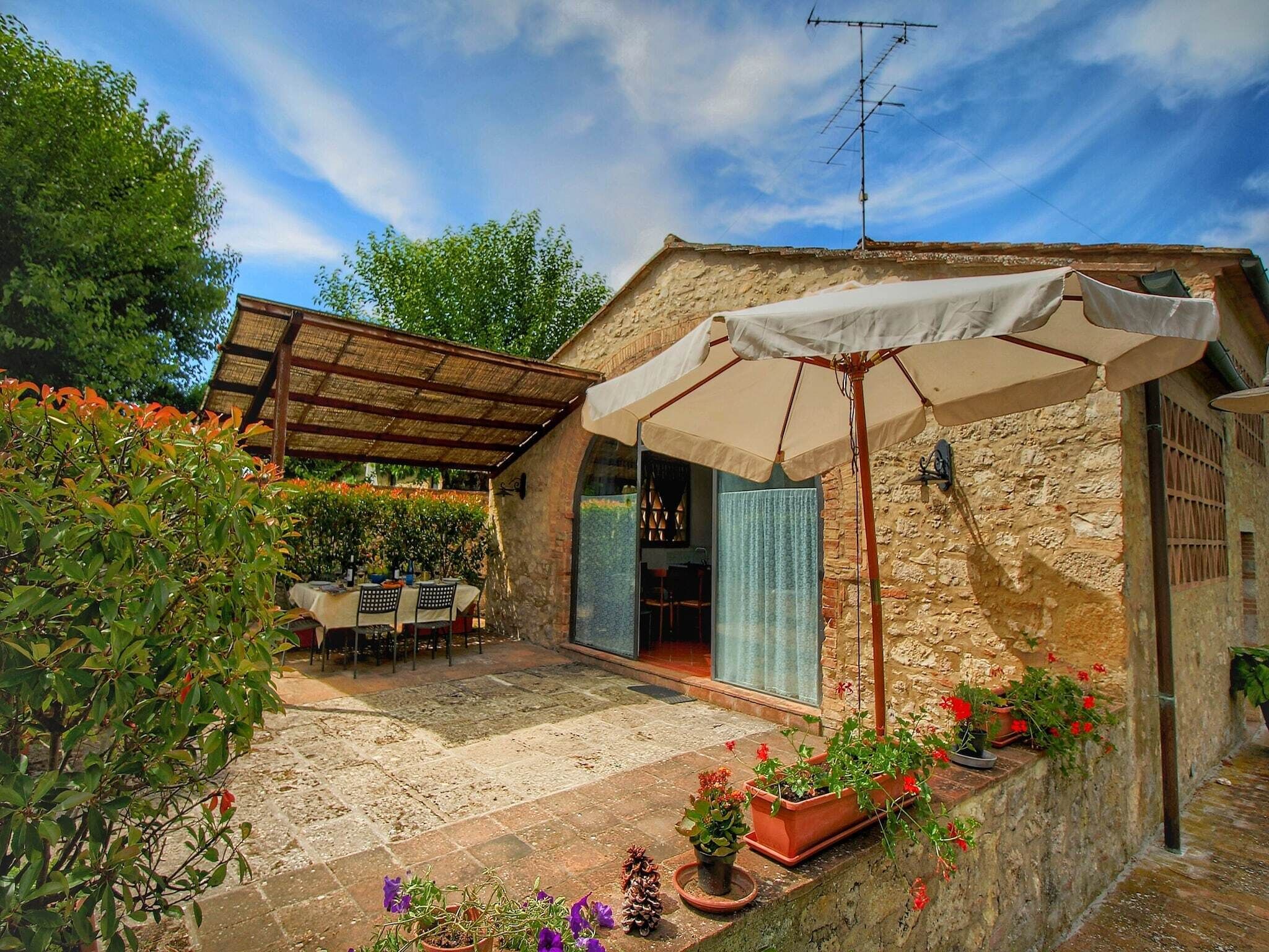 Ein Steinhaus mit überdachter Terrasse, Außenbestuhlung und Topfpflanzen.