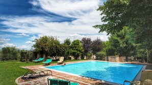 Une piscine rectangulaire, bordée d’une terrasse carrelée et entourée d’une pelouse verdoyante et d’arbres.