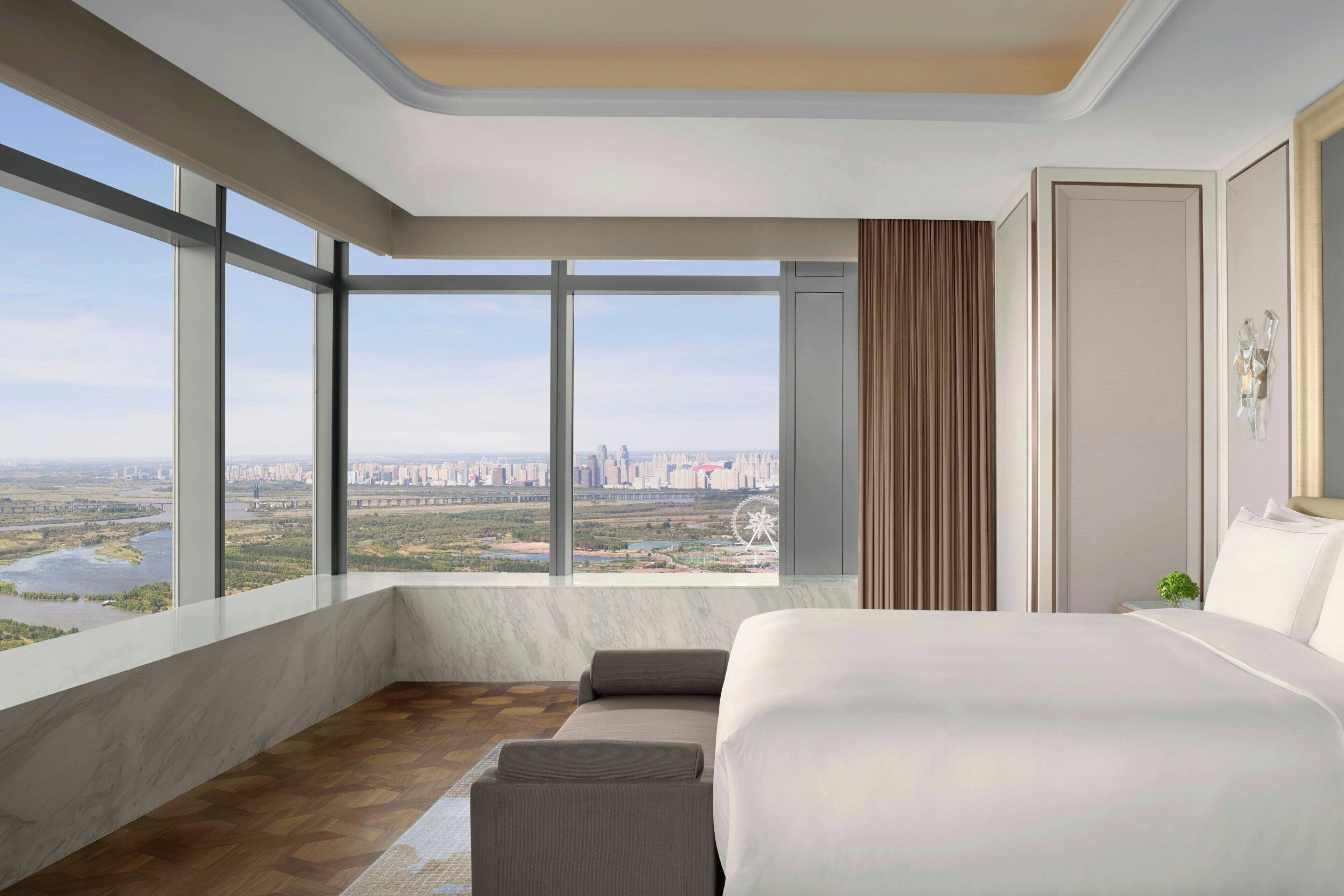 Habitación de hotel moderna con una cama grande, vista a la ciudad y un ventanal amplio.