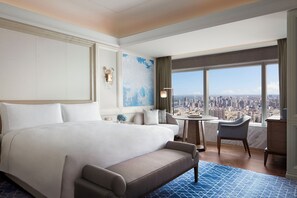 A hotel room with a large bed, a seating area with a view of the city, and a small table with a lamp.